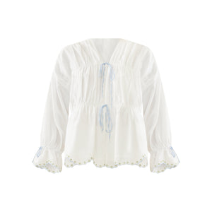 Front view of Isle top in White Whimsy with V-neck, two blue tie closures, peplum waist, puff sleeves, scalloped embroidered hem