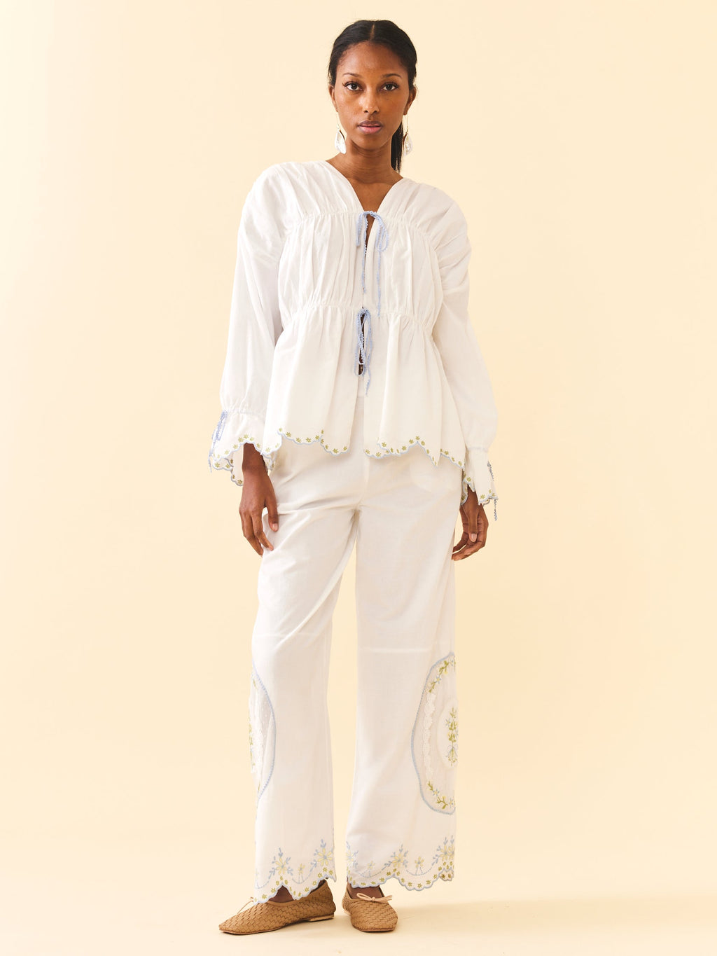 Front view of Isle Top in White Whimsy showcasing front ties, gathered peplum waist, long puff sleeves, and scalloped embroidered hem on a cream background