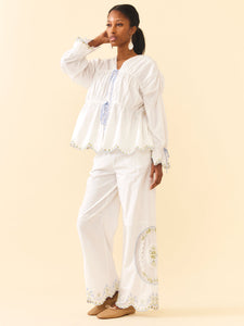 Three-quarter view of Isle Top in White Whimsy on model, loose fit with tie-front and scalloped embroidered hem against cream