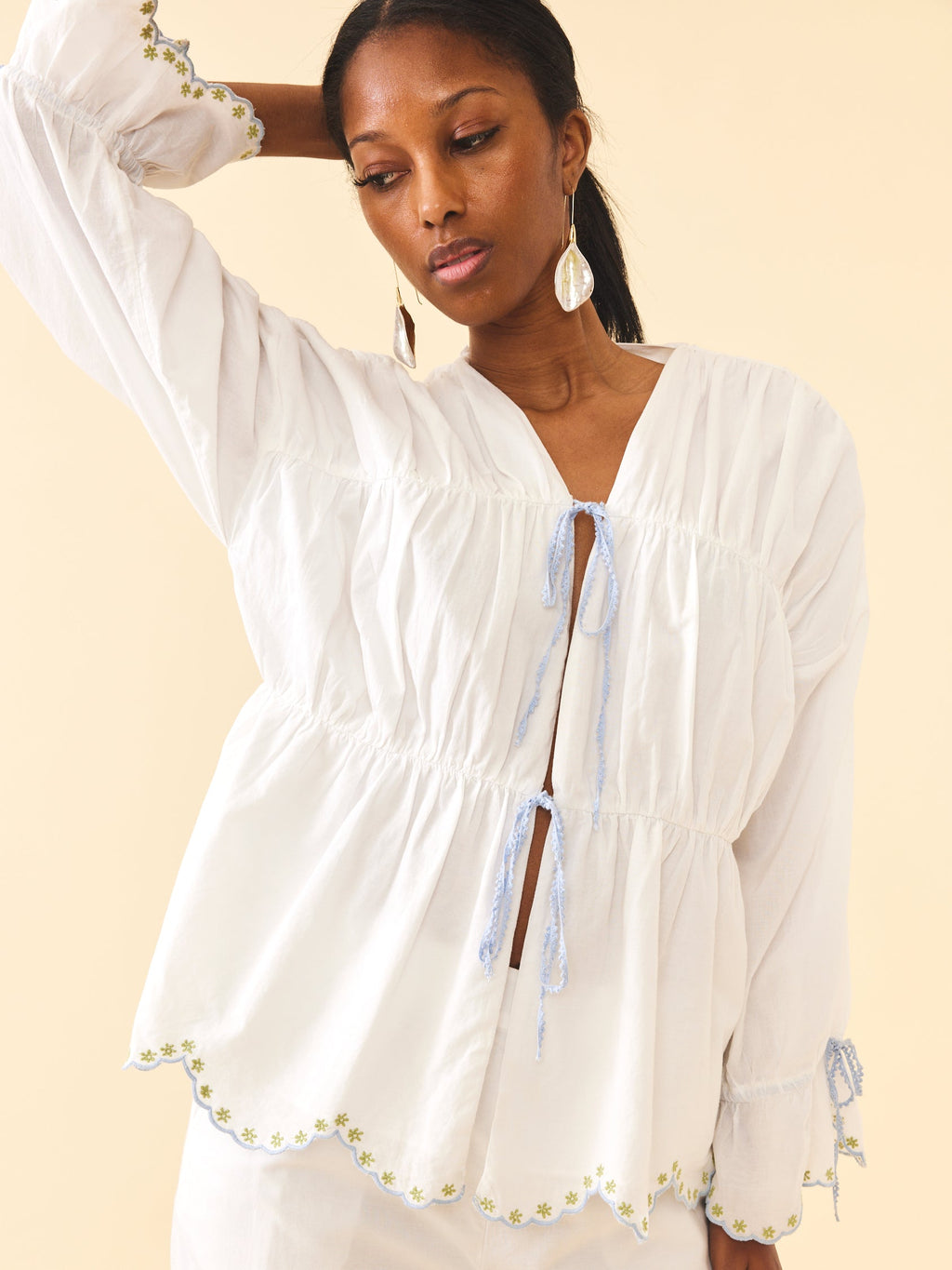 Three-quarter view of Isle Top in White Whimsy showing tie-front tiers, scalloped embroidered hem on pale beige background