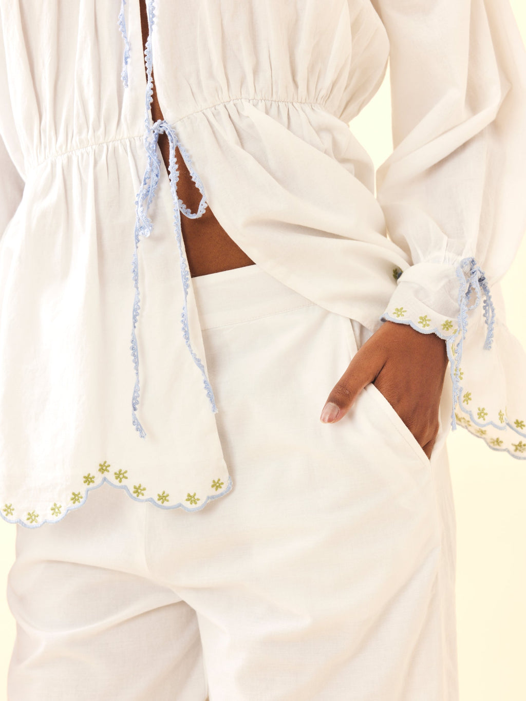Close-up of Isle Top in White Whimsy showing scalloped embroidered hem, blue tie trim, gathered waist and puff sleeve