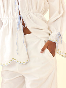 Close-up of Isle Top in White Whimsy showing scalloped embroidered hem, blue tie trim, gathered waist and puff sleeve