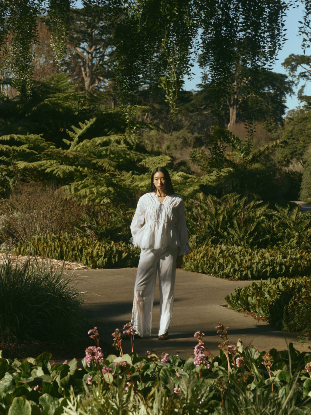 Front view of Isle Top in White Whimsy on model showcasing billowy long sleeves, embroidered eyelet details, and scalloped hem in a garden setting