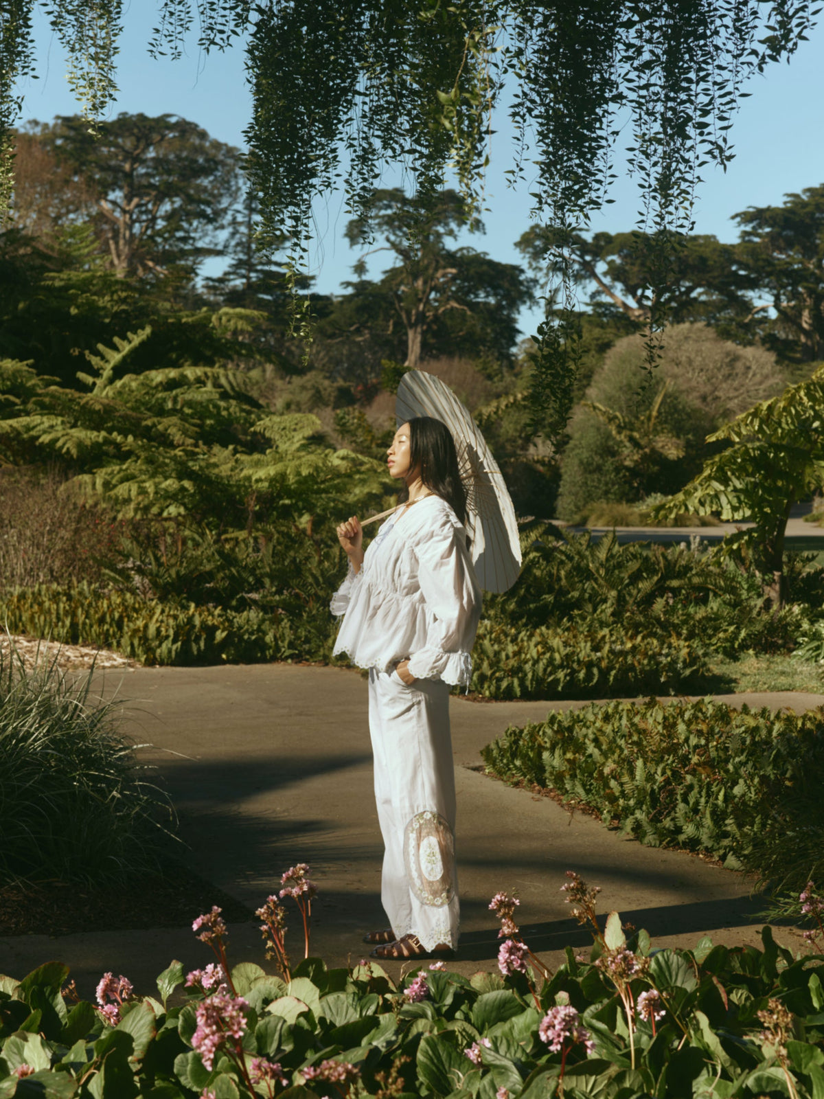 Side profile of Isle Top in White Whimsy on model showing billowy peasant silhouette, lace trim, and puff sleeves in a garden