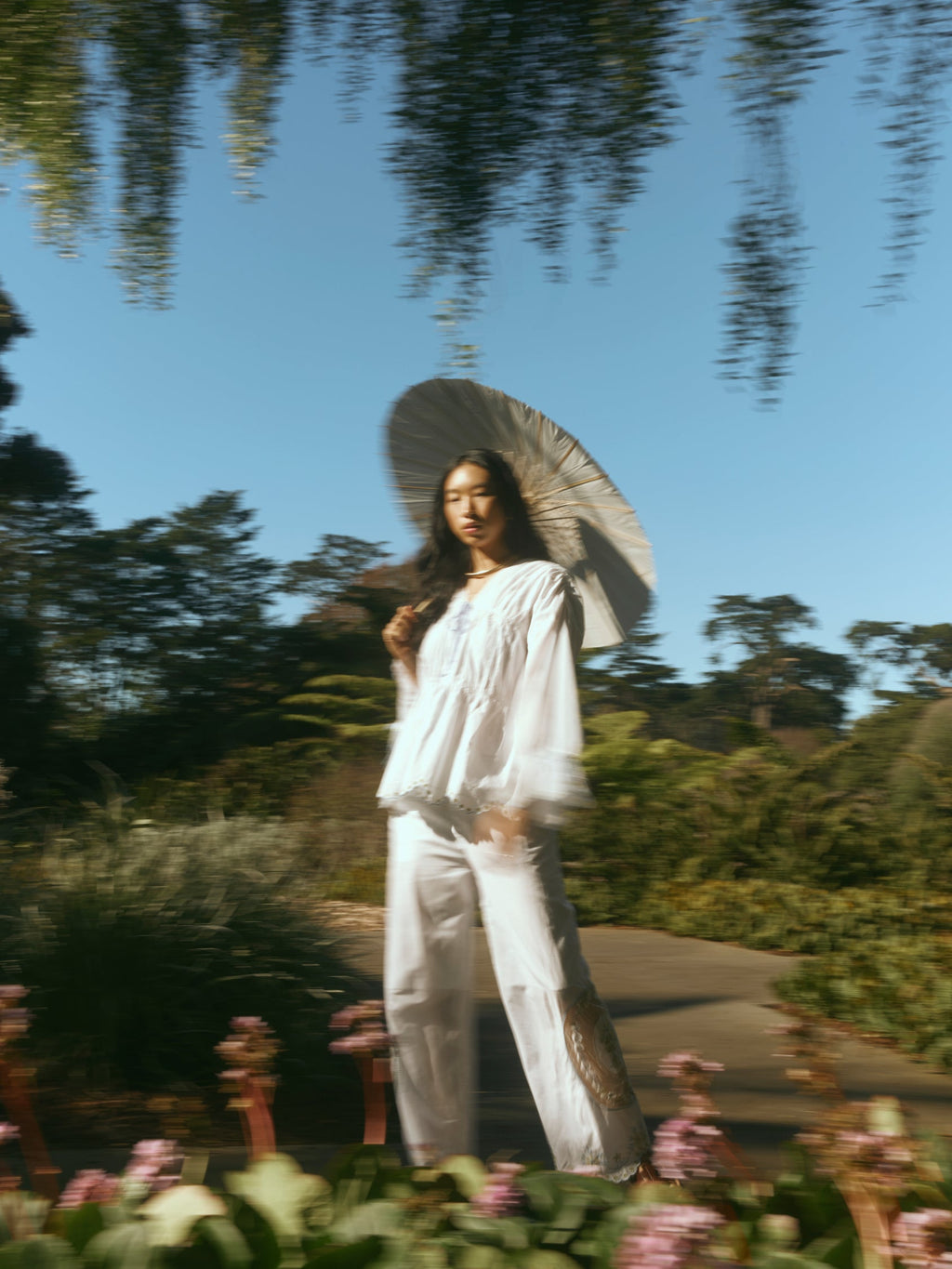 Three-quarter view of Isle Top in White Whimsy on model, billowy long sleeves and lace pintuck details, garden path