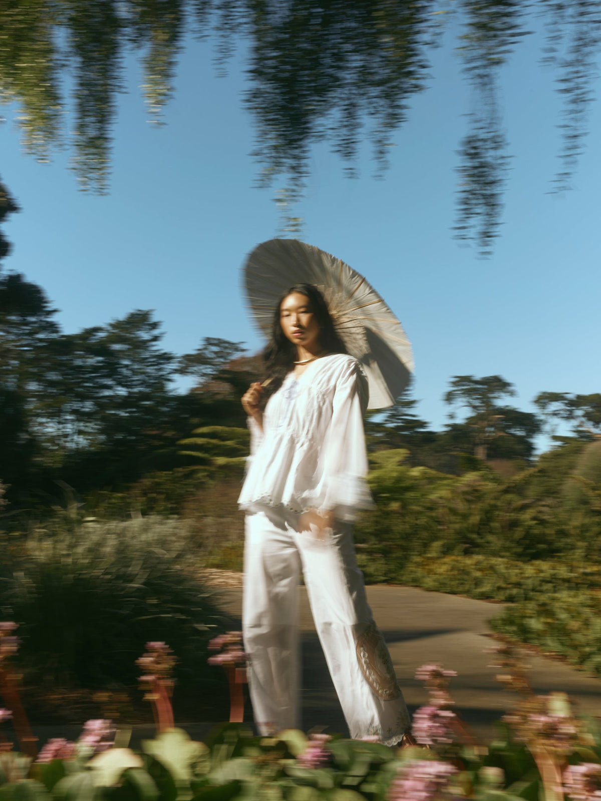 Three-quarter view of Isle Top in White Whimsy on model, billowy long sleeves and lace pintuck details, garden path