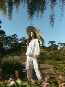 Three-quarter view of Isle Top in White Whimsy on model, billowy long sleeves and lace pintuck details, garden path