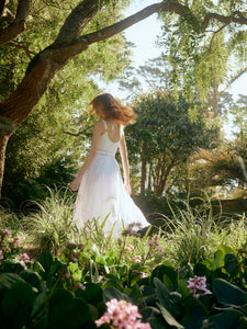 Model twirling in a white Katherine midi dress with lace embroidery and adjustable straps in a sunlit garden