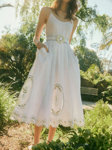 Front view of Katherine dress in White Whimsy with belted waist, side pockets, embroidered scalloped hem in a sunlit garden