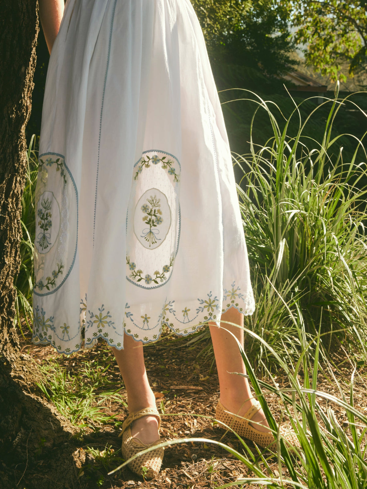 Front view of Katherine Dress in White Whimsy showing midi A-line skirt with blue-green floral embroidery and scalloped hem outdoors