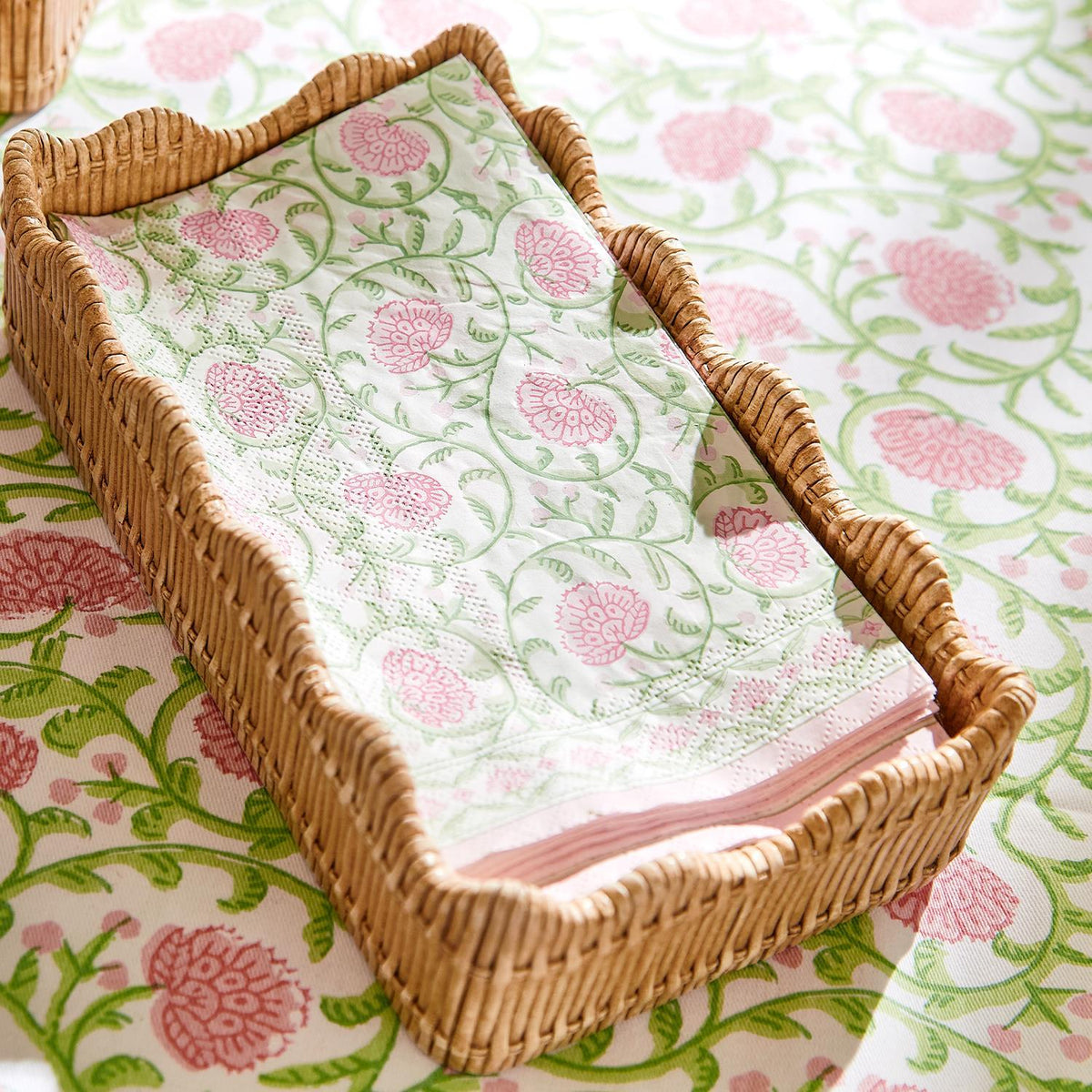 Angled view of scalloped-edge woven napkin holder with basket-weave texture holding pink floral napkins on matching cloth