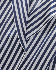 A close-up of Petite Plumes Womens Silk Robe in Navy Bengal Stripe shows folded Mulberry silk fabric with diagonal stripes, creating a textured pattern that highlights the color contrast and sheen, reminiscent of luxurious sleepwear.