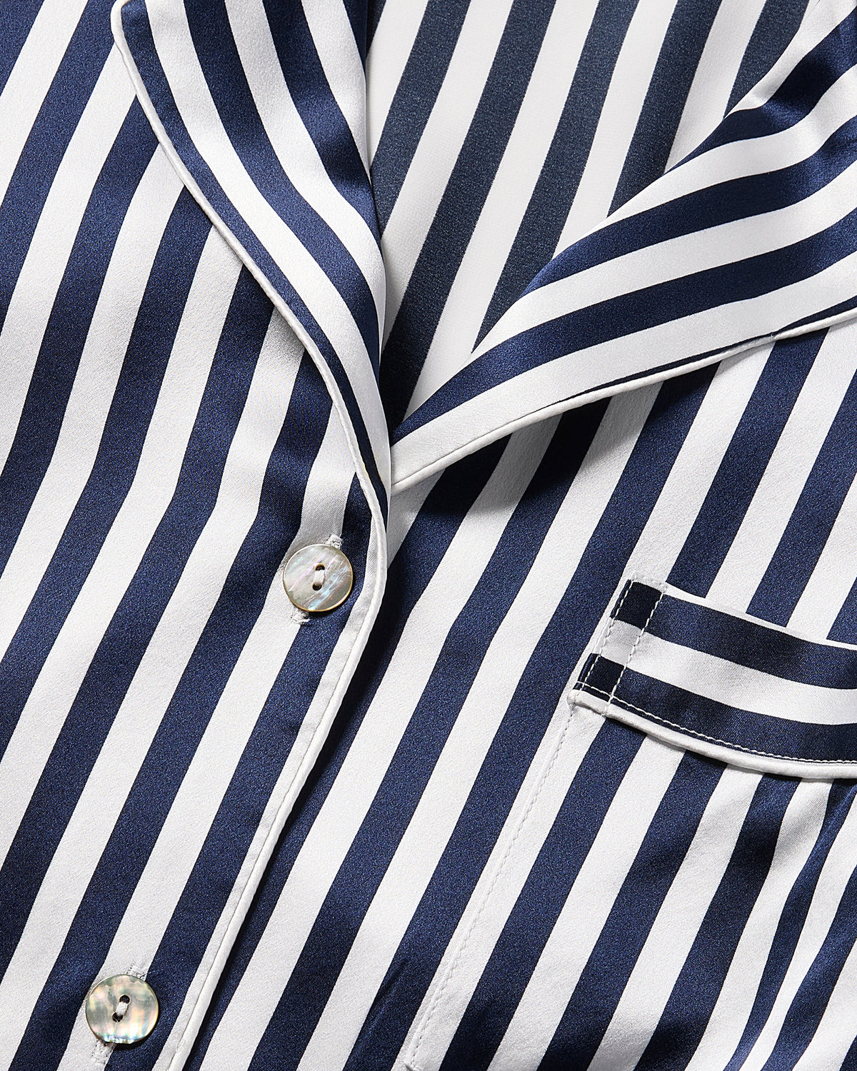 The Womens Silk Short Set by Petite Plume features a striped pajama top with navy Bengal and white vertical lines. It includes a collar, buttons, and a right-side pocket with matching trim, offering smooth, shiny luxury sleepwear in silk.