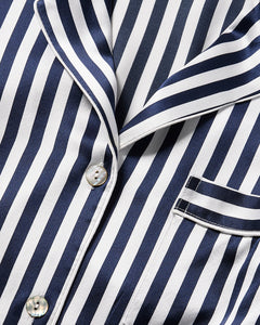 The Womens Silk Short Set by Petite Plume features a striped pajama top with navy Bengal and white vertical lines. It includes a collar, buttons, and a right-side pocket with matching trim, offering smooth, shiny luxury sleepwear in silk.