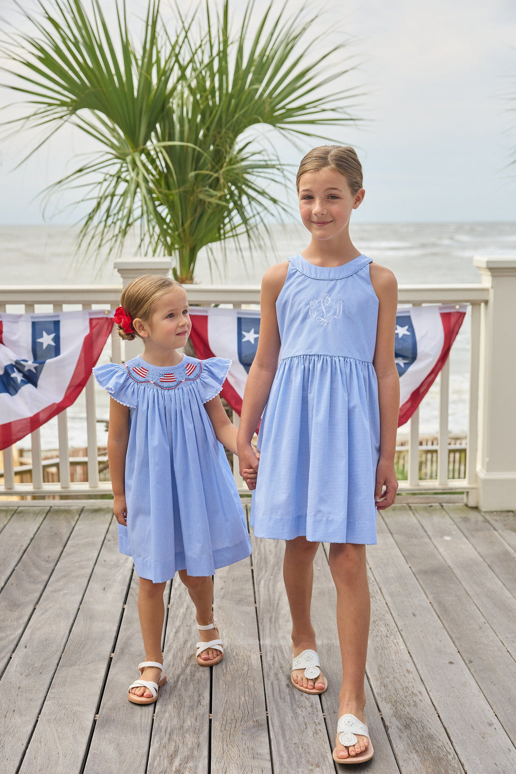 Little English traditional children's clothing. Flutter sleeve dress for toddler girls in royal blue mini gingham with smocking at the collar and American flag bunting