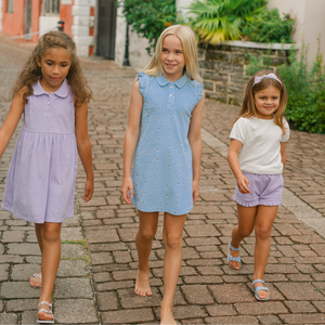 Three girls walking on a cobblestone street, center girl wearing light blue floral French terry dress with ruffle sleeves