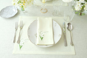 Flat lay of Lily of the Valley napkin and placemat set showcasing embroidered lily-of-the-valley motif on light green linen