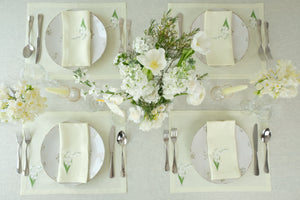 Top-down view of Lily of the Valley napkin and placemat set showcasing light green linen with floral embroidery on a table