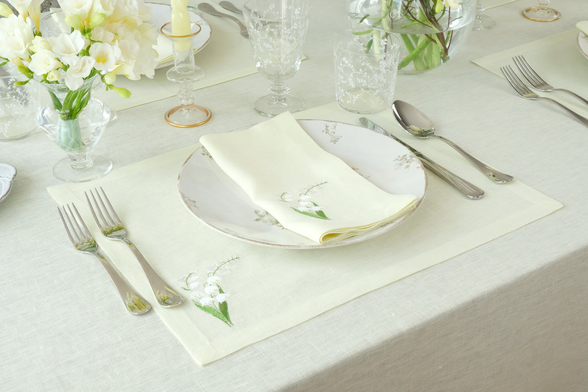 Top-down view of Lily of the Valley napkin and placemat set showcasing embroidered lily of the valley motif on light green linen with plate and silverware