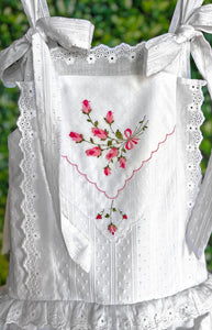 Close-up of Heirloom Handkerchief drop-waist dress with pink rose embroidery on the bodice, eyelet trim, and tied ribbon straps