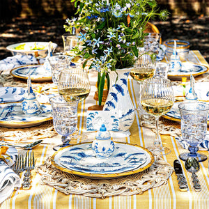 Place card holders and matching blue-and-white Country Estate plates arranged on an outdoor dining table with yellow striped tablecloth and floral centerpiece