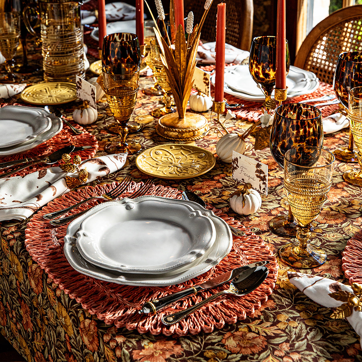 Autumn table with sepia place cards in mini pumpkin holders, white scalloped plates, amber glassware, and rust placemats