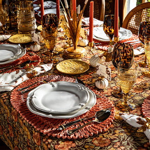 Autumn table with sepia place cards in mini pumpkin holders, white scalloped plates, amber glassware, and rust placemats
