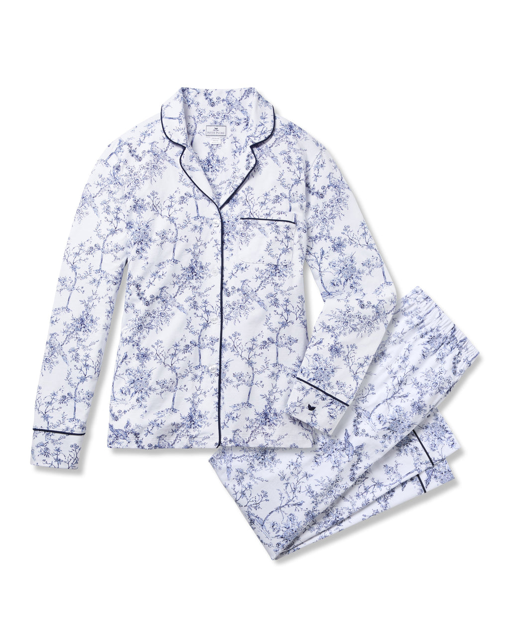 The Womens Pima Pajama Set in Timeless Toile by Petite Plume is a white sleepwear ensemble featuring a blue floral print. It includes a long-sleeved button-up top with chest pocket and matching pants, accented with dark trim for added classic elegance.