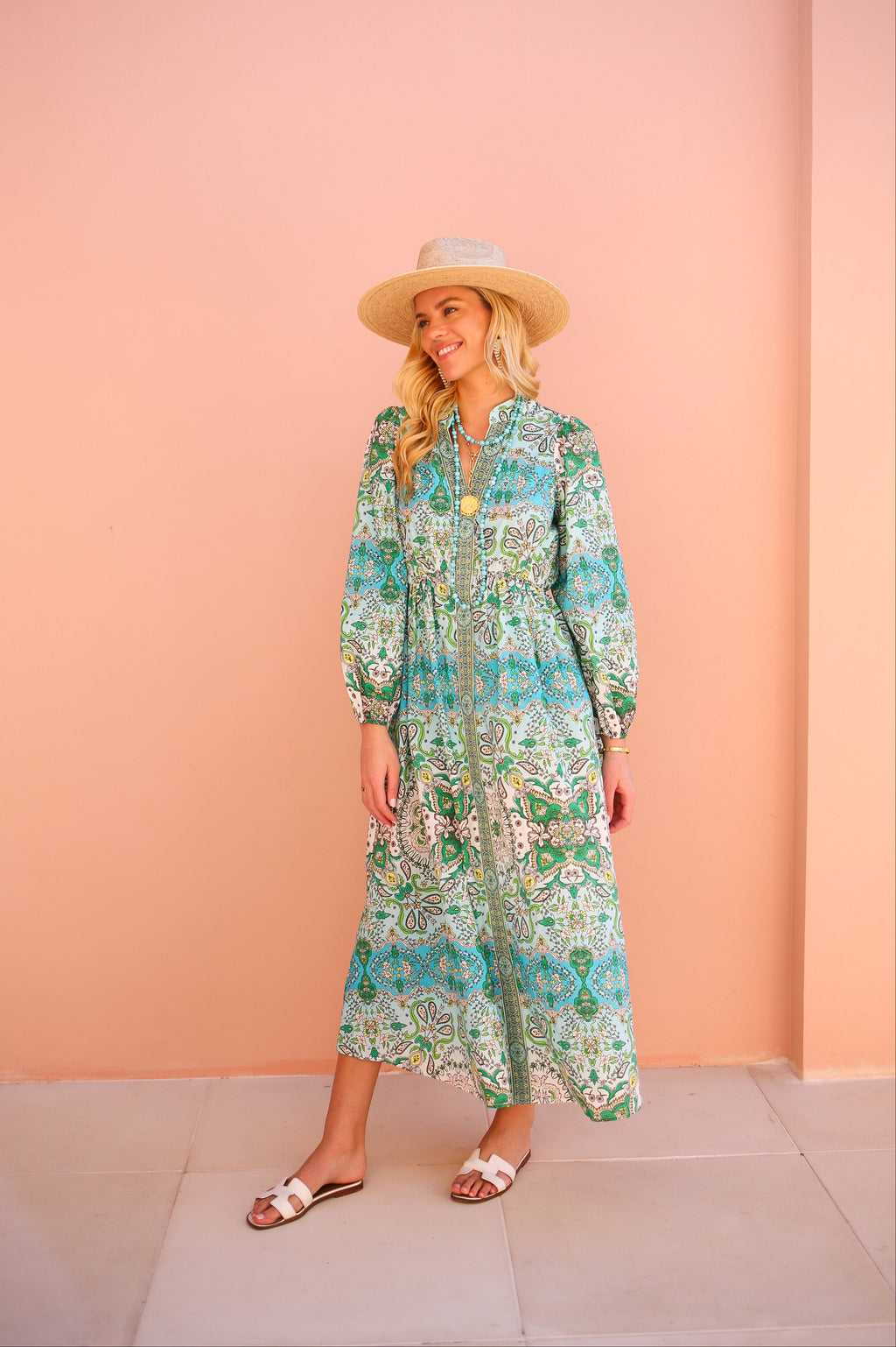 Woman wearing a floral dress and hat against a pink wall