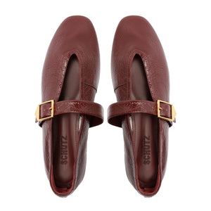 Top view of Courtney Buckle patent flat in vino showcasing square toe, gold buckle strap, and pebbled patent leather on white background
