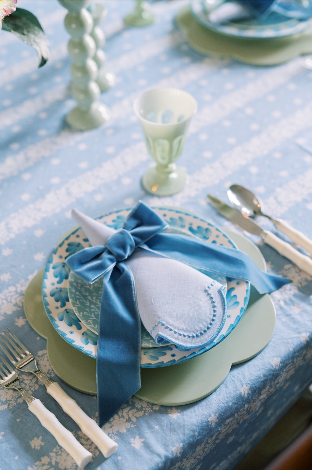 Close-up of blue-dotted white linen napkin on scalloped placemat, napkin tied with blue velvet bow on blue tablecloth
