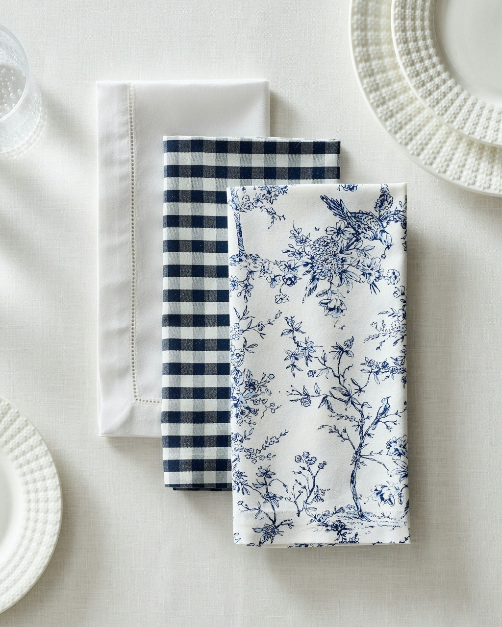 Top view of Signature Twill napkins showing white hemstitched, navy gingham, and navy toile patterns on a white tablecloth
