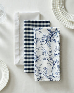 Top view of Signature Twill napkins showing white hemstitched, navy gingham, and navy toile patterns on a white tablecloth
