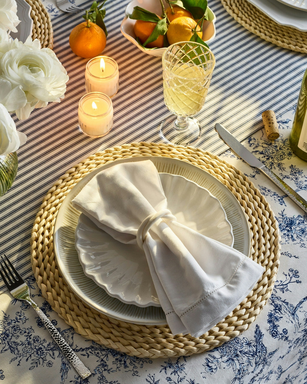 Top-down view of Signature Twill napkin folded with napkin ring on stacked plates over navy-striped French ticking tablecloth