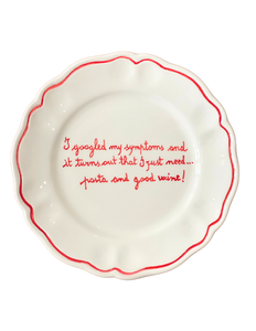 Top view white scalloped ceramic plate with red rim and handwritten joke about needing pasta and wine on black background