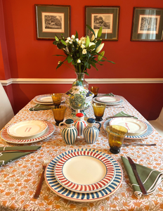 Top view of scalloped ceramic plates showing red and blue striped rims on table with amber glasses and floral vase