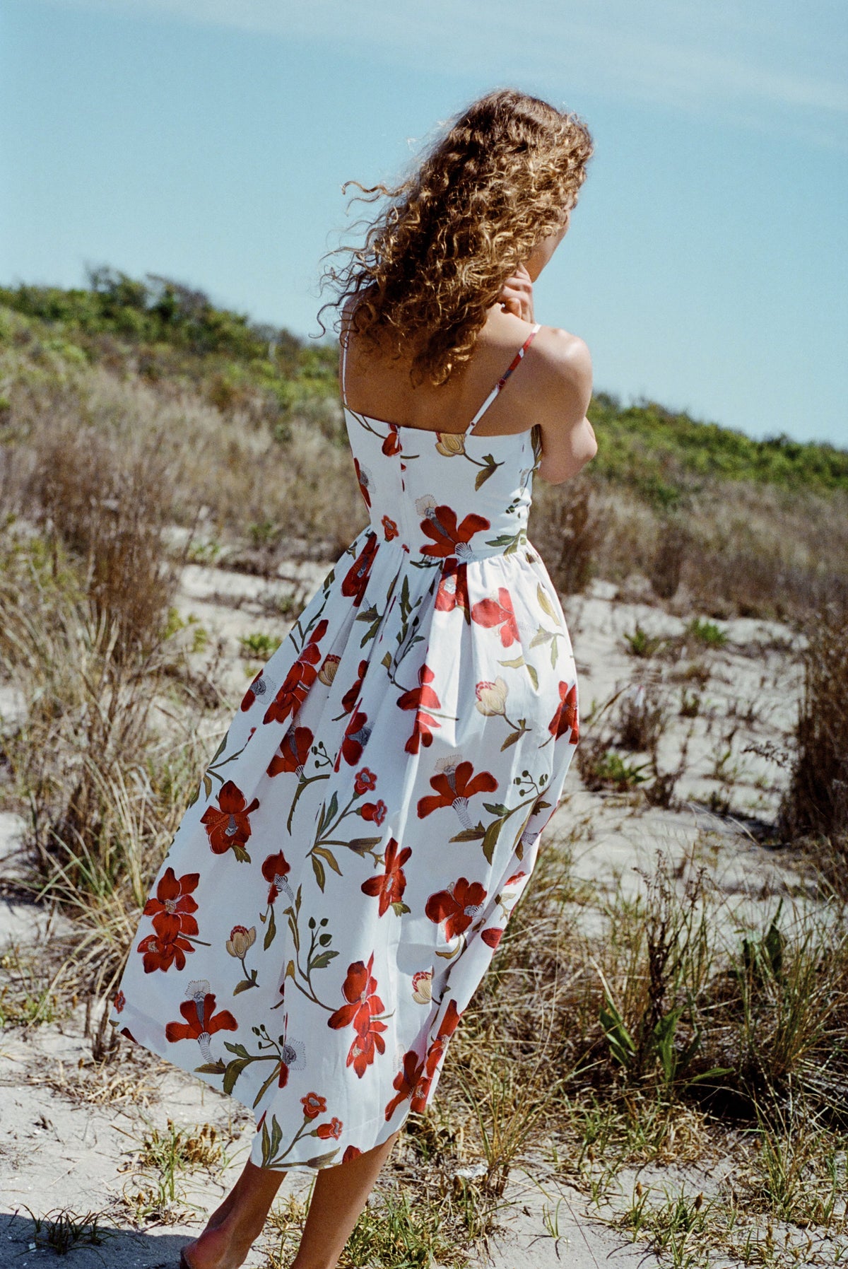 Back view of Skinny-Strap Poof Dress in Red Hibiscus with adjustable straps, fitted waist, and full floral skirt on sand