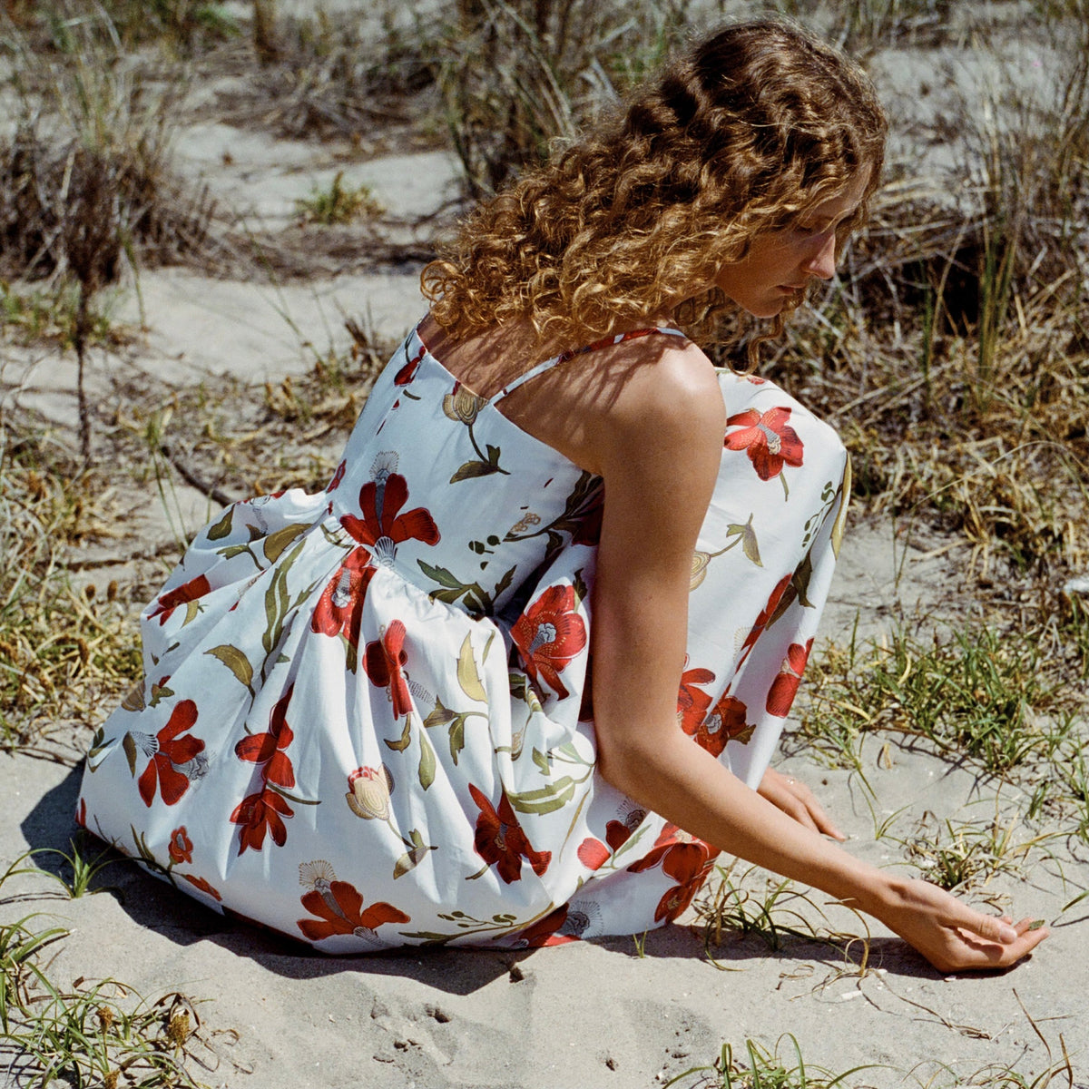 Back three-quarter view of Skinny-Strap Poof Dress in Red Hibiscus showing straps, fitted waist and full floral skirt on sand