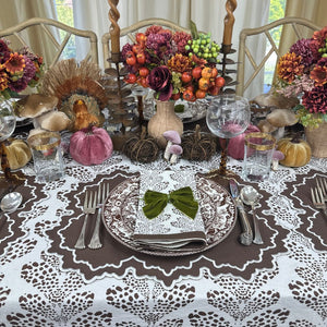 Decorative table setting with pumpkins, flowers, and cutlery on a patterned tablecloth. Luxury embroidered placemat and block print napkin