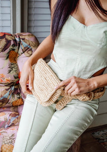 Model sitting and wearing straw belt bag at waist