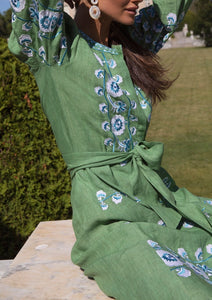 Three-quarter view of Emerald Lucia Dress on model showing emerald linen with blue-white floral embroidery and tied waist belt outdoors