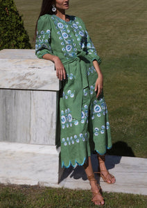 Three-quarter view of Emerald Lucia dress showcasing blue floral embroidery, scalloped hem and tie belt by a marble ledge