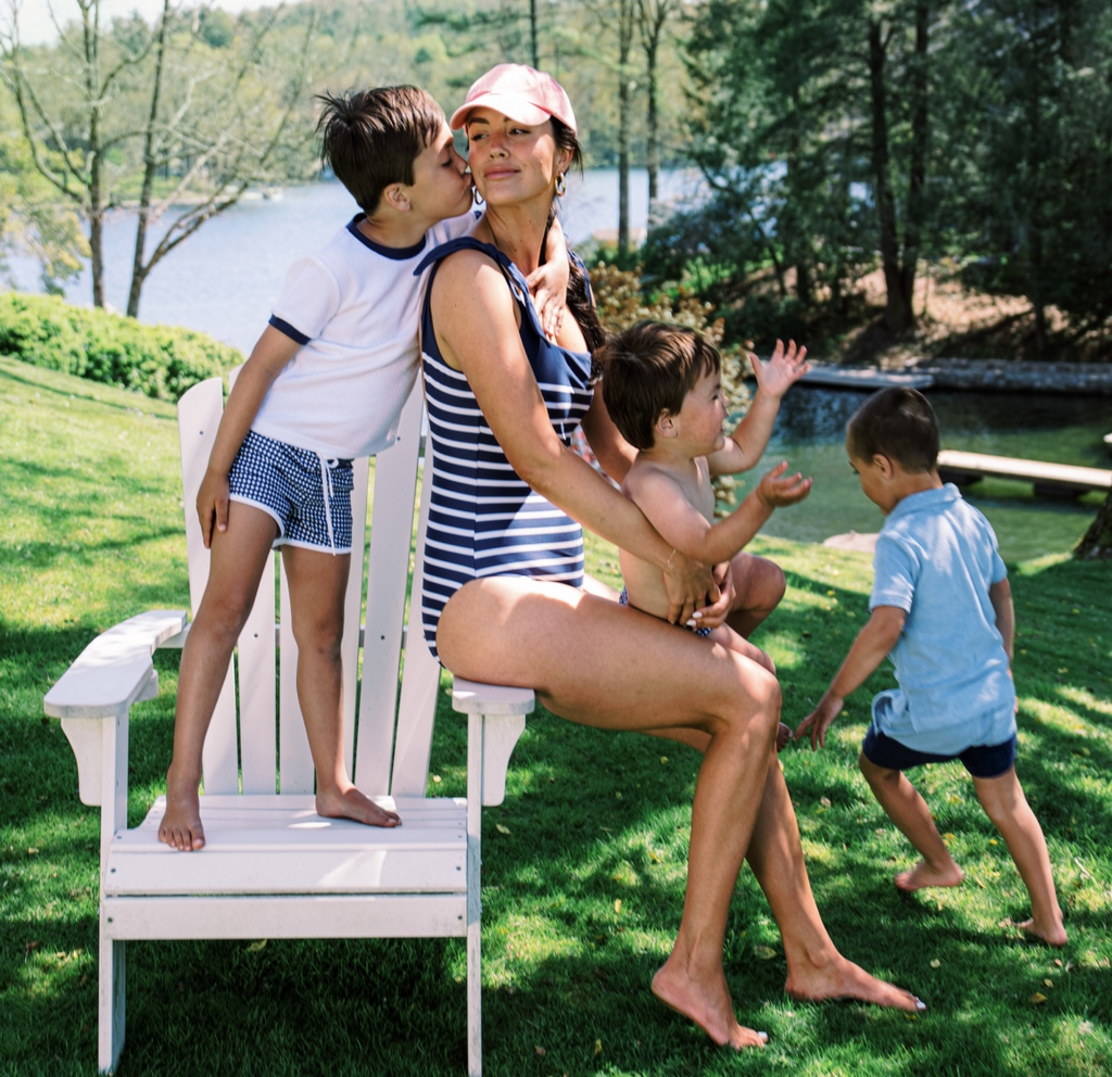 Woman in navy Breton-striped tie-knot one-piece swimsuit seated by a lake with three children