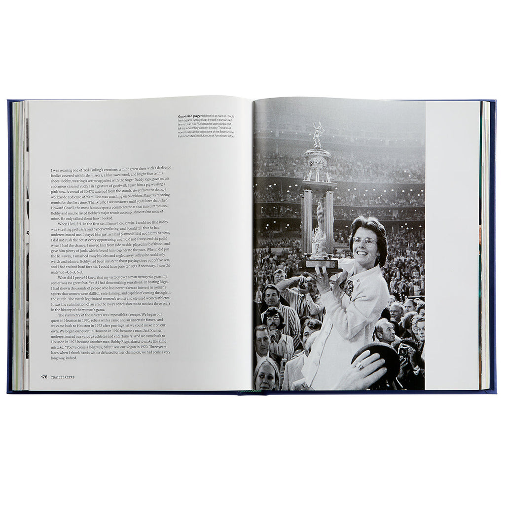 Top-down view of open book ‘Trailblazers: The Unmatched Story of Women’s Tennis’ showing a two-page spread with black-and-white trophy photo and text, blue cover edges visible