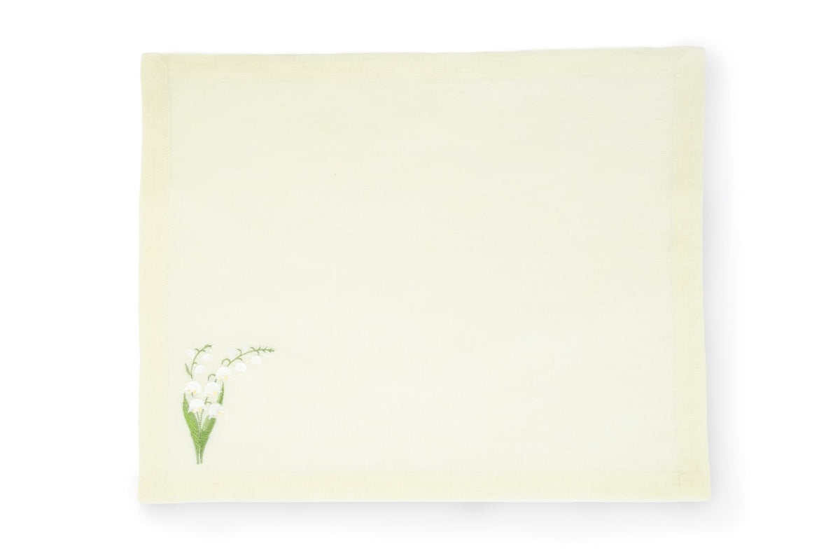 Flat lay of light green linen placemat with small embroidered lily-of-the-valley motif at lower-left on white background