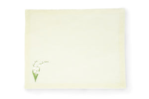 Flat lay of light green linen placemat with small embroidered lily-of-the-valley motif at lower-left on white background