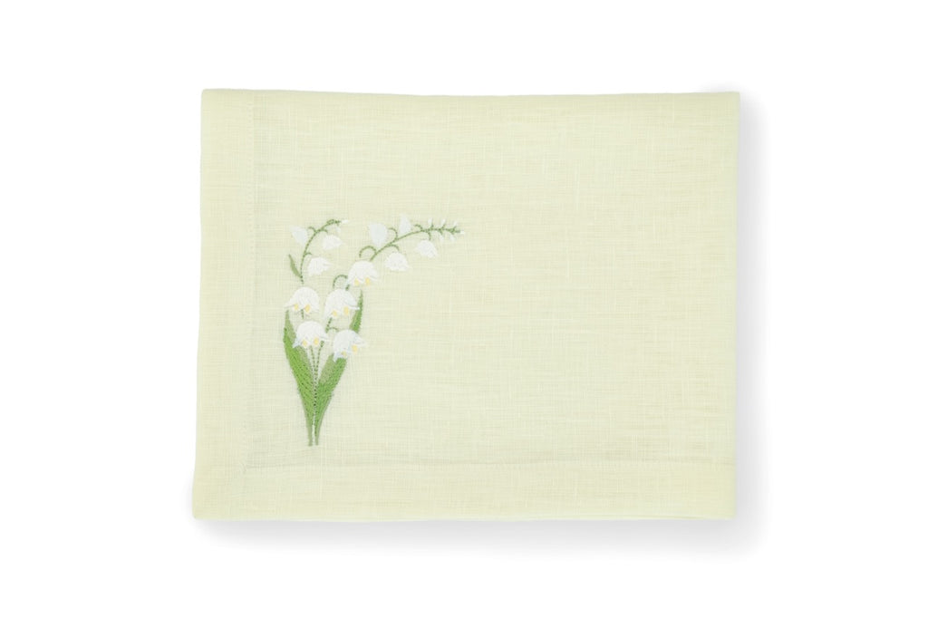 Top view of folded light green linen napkin showcasing embroidered white lily of the valley motif on lower left