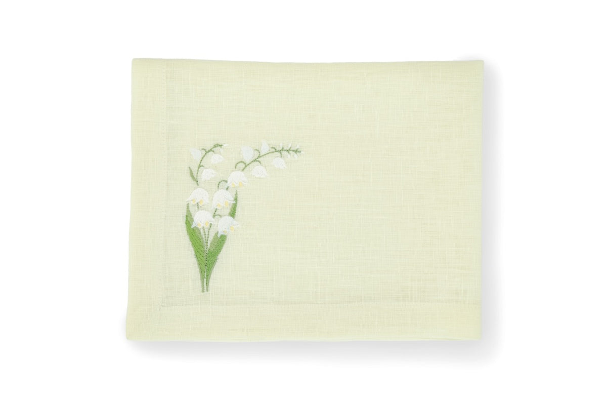 Top view of folded light green linen napkin showcasing embroidered white lily of the valley motif on lower left