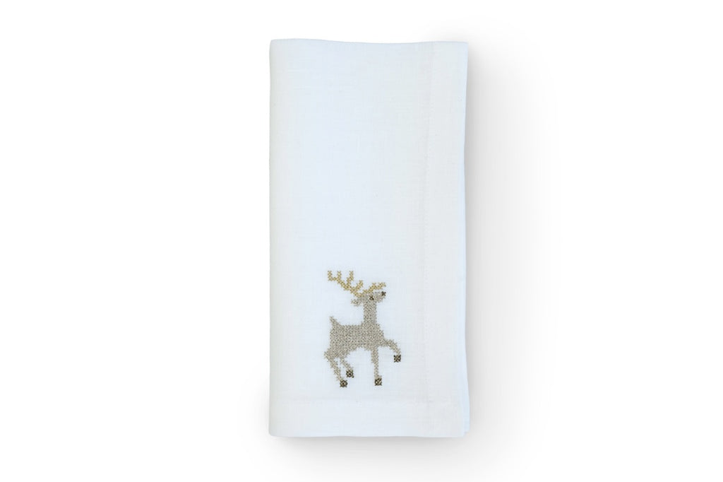 Top-down view of folded white linen napkin showcasing gold sparkling reindeer embroidery on white background
