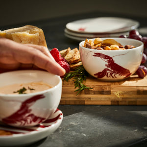 A Red Lobster Snack Bowl from Caskata holds nuts on a wooden charcuterie board.